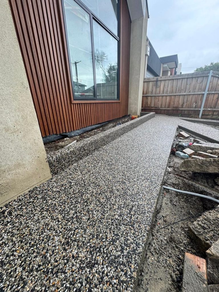 Close-up of an exposed aggregate side path beside a timber-clad home in Melbourne